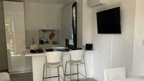 A modern kitchen with a central island, white bar stools, a flat-screen TV mounted on the wall, and a dining table with chairs. - Magda's Corner-directly on the lake-private beach is private parking (Lombardia)