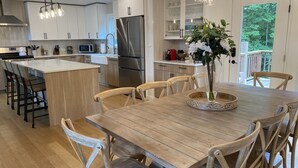 Moderni keittiö, jossa on keskellä sijaitseva saareke, puiset tuolit ja ruokapöytä, jonka päällä on maljakko täynnä kukkia.