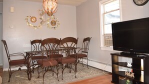A dining area with a chandelier, a clock, and a television on a stand.