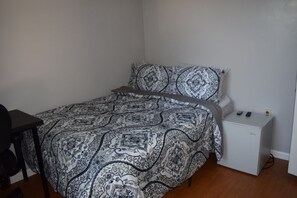 A bedroom with a patterned bedspread, a small white dresser, and a desk with a chair.