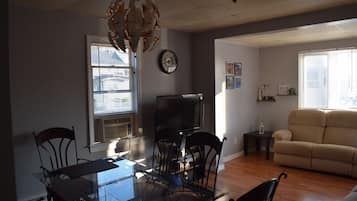 Una sala de estar con sofá, televisión y comedor con sillas y mesa.