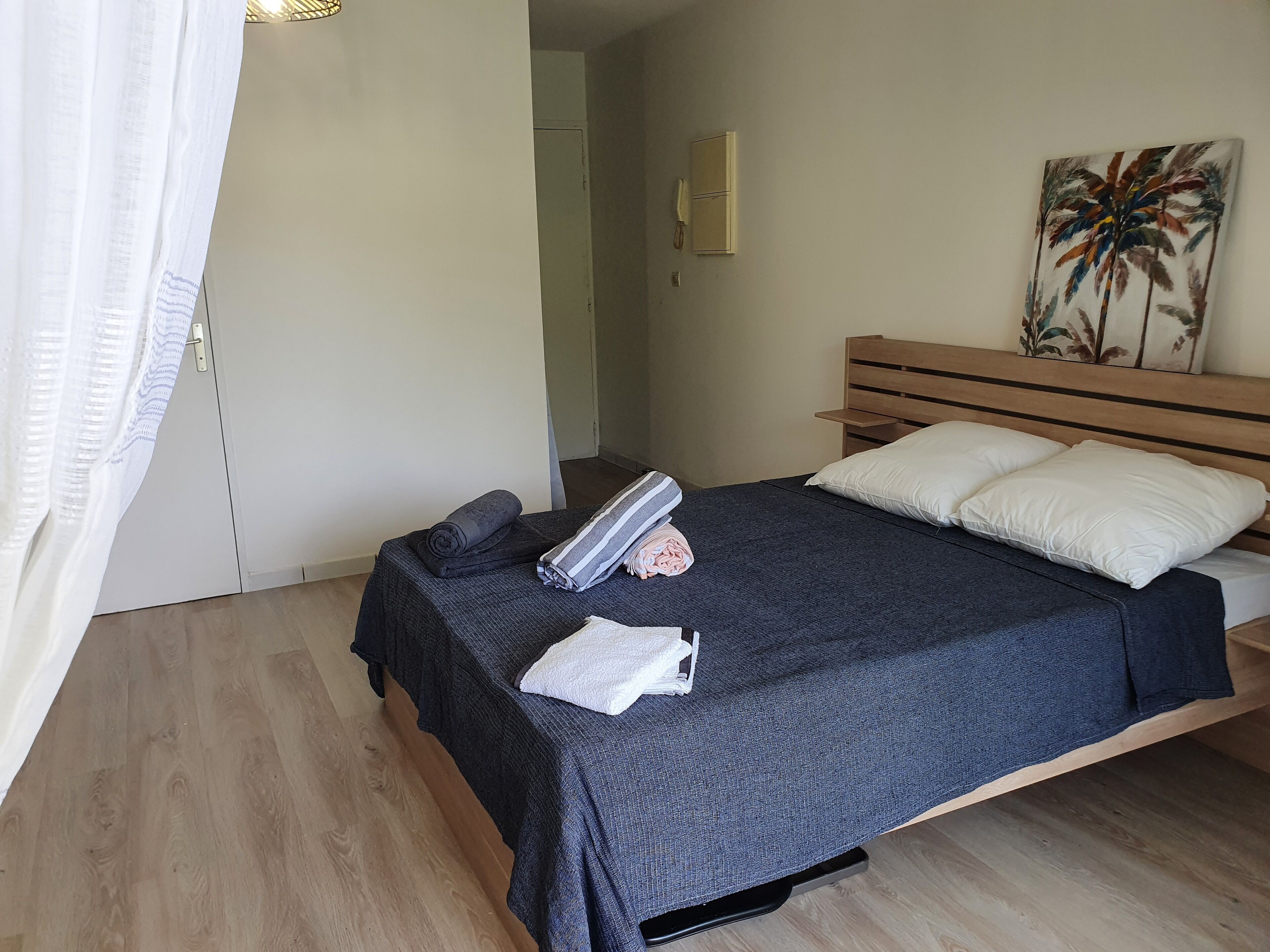 A bedroom with a bed, a wooden headboard, a nightstand, a painting, and a door with a curtain.