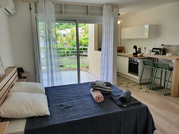 Un dormitorio con cama, escritorio y vista a un jardín por un ventanal corredero.