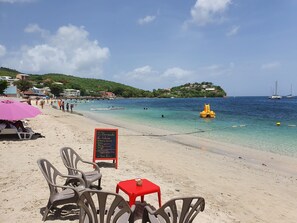 Una playa con agua cristalina, un boya amarillo y un cartel rojo.