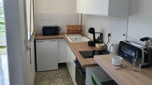 A compact kitchen with a microwave, toaster, and kettle on the counter, a small sink, and a wooden drying rack.