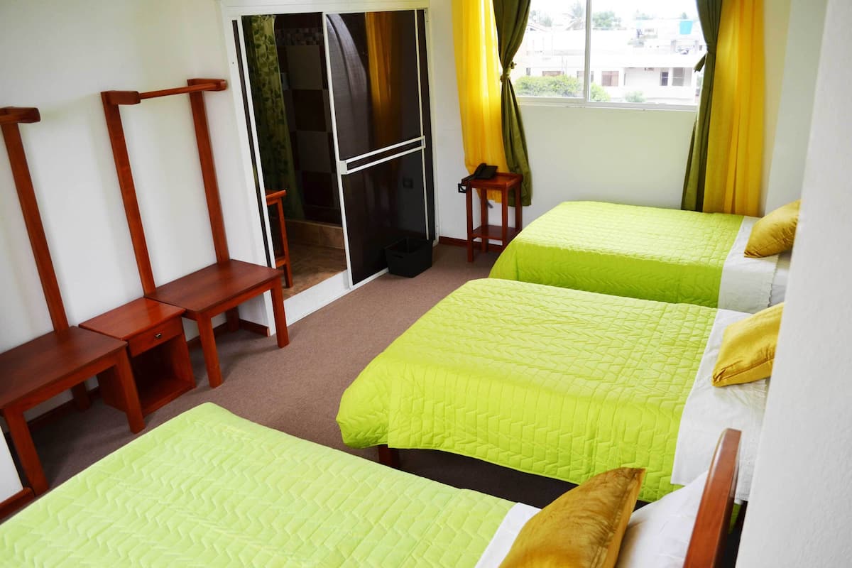 A hotel room with two beds, wooden furniture, a small table, and a window with curtains.