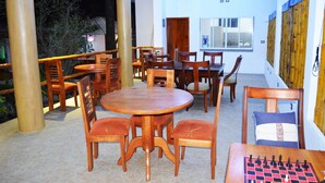 A dining area with wooden tables and chairs, a chessboard, and a window with a view of the outside. - Isla Azul Hotel (Puerto Ayora)