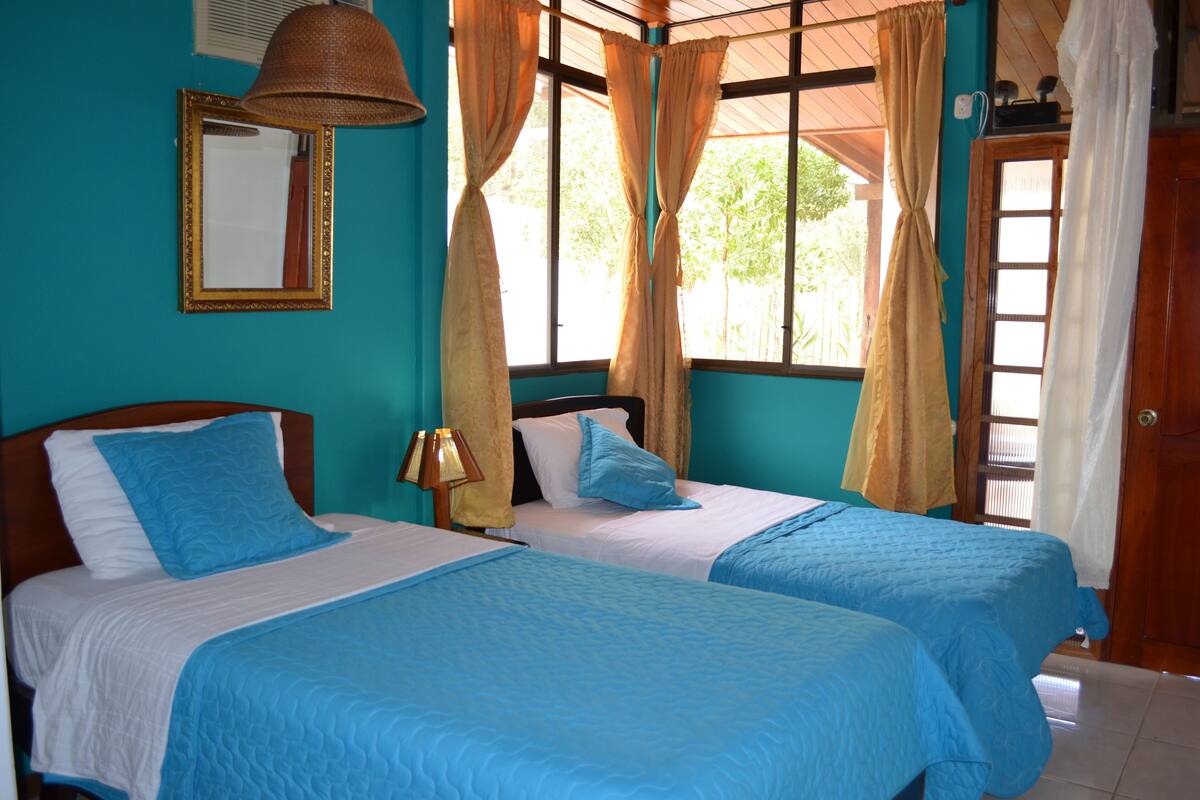 A room with two beds, a mirror, and a window with curtains.