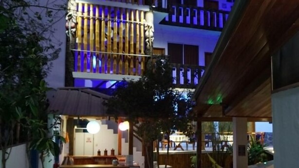 A courtyard with a reception desk, a bicycle, and a building with vertical wooden slats and blue lighting. - Isla Azul Hotel (Puerto Ayora)