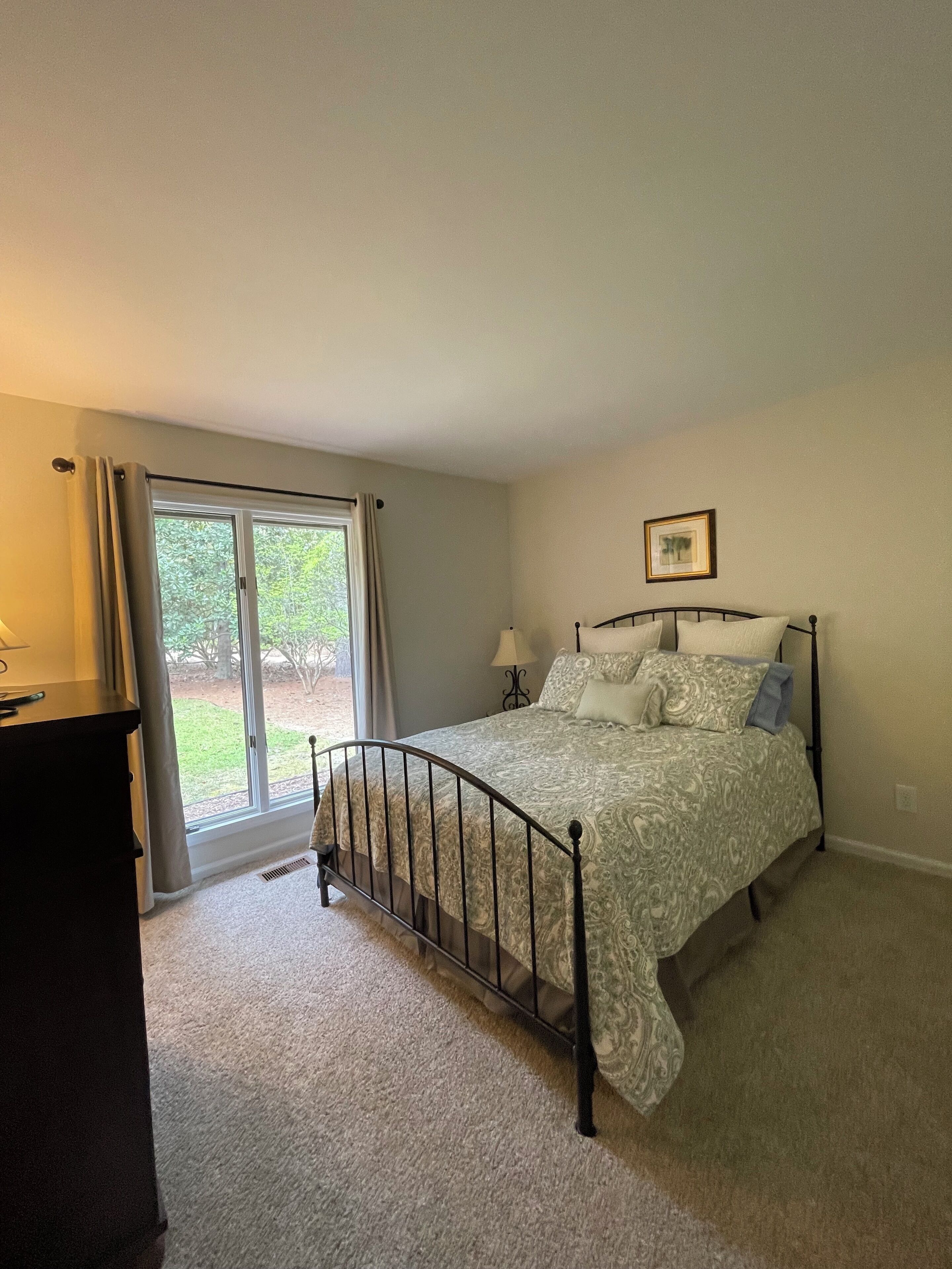 A bedroom with a bed, a window with curtains, a bedside table, and a picture on the wall.