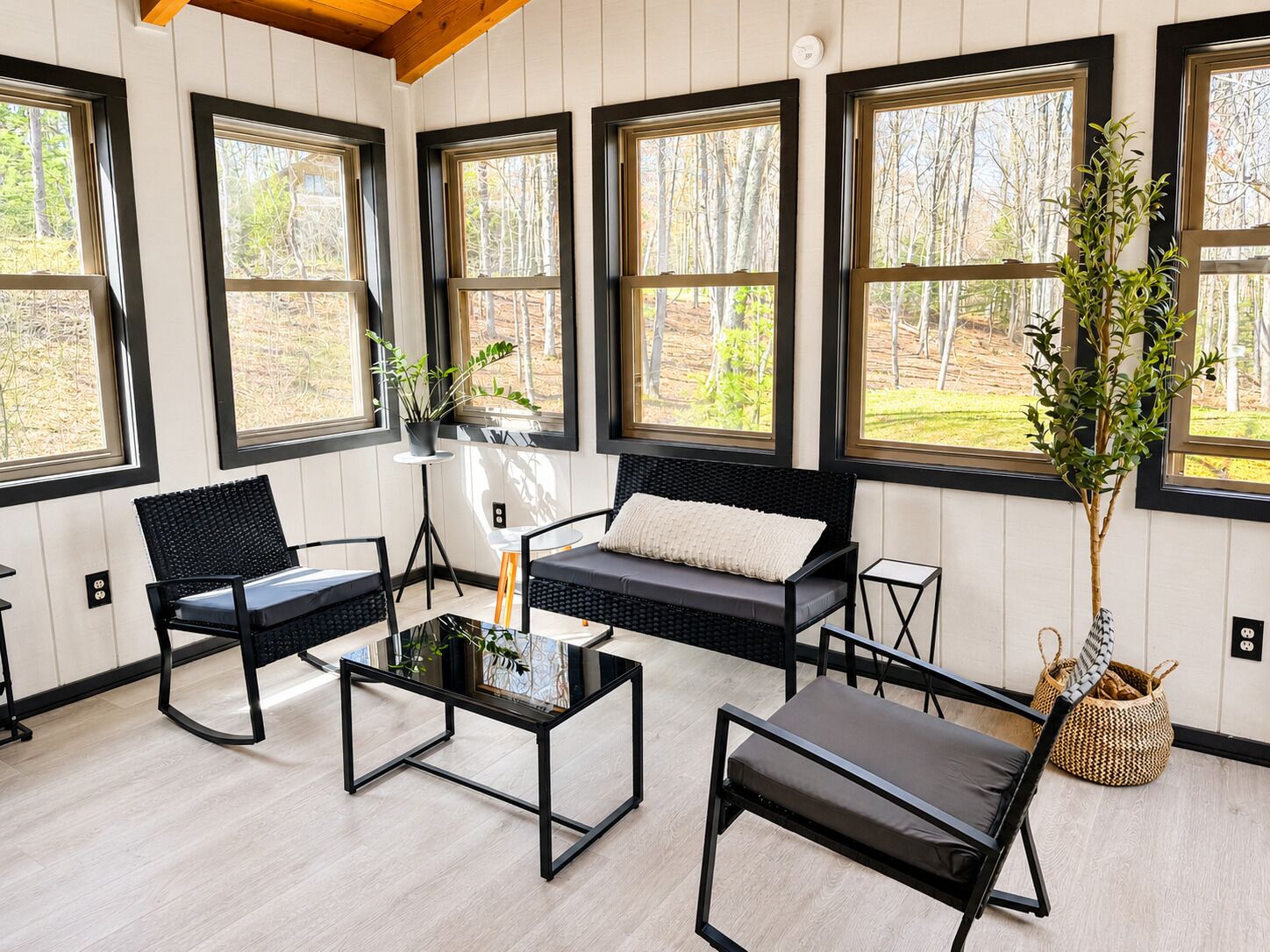 Et moderne interiør med store vinduer, en sort sofa, et glas sofabord og sorte stole.