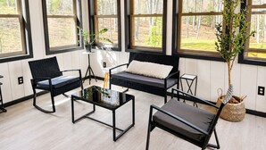 Moderni sisustus, jossa on suuret ikkunat, musta sohva, lasinen sohvapöytä ja mustat tuolit.