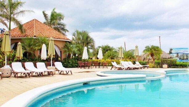 A pool area with lounge chairs and umbrellas, surrounded by palm trees and a building with a tiled roof. - Suite San Juan 125 Gran Pacifica Resort (Villa El Carmen)