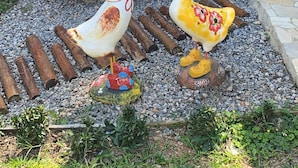 Un jardín con dos grandes esculturas de patos, una hamaca y un muro de ladrillo con una ventana.