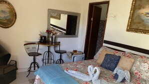 Una habitación de hotel con cama, escritorio con silla, un refrigerador pequeño y un espejo en la pared.