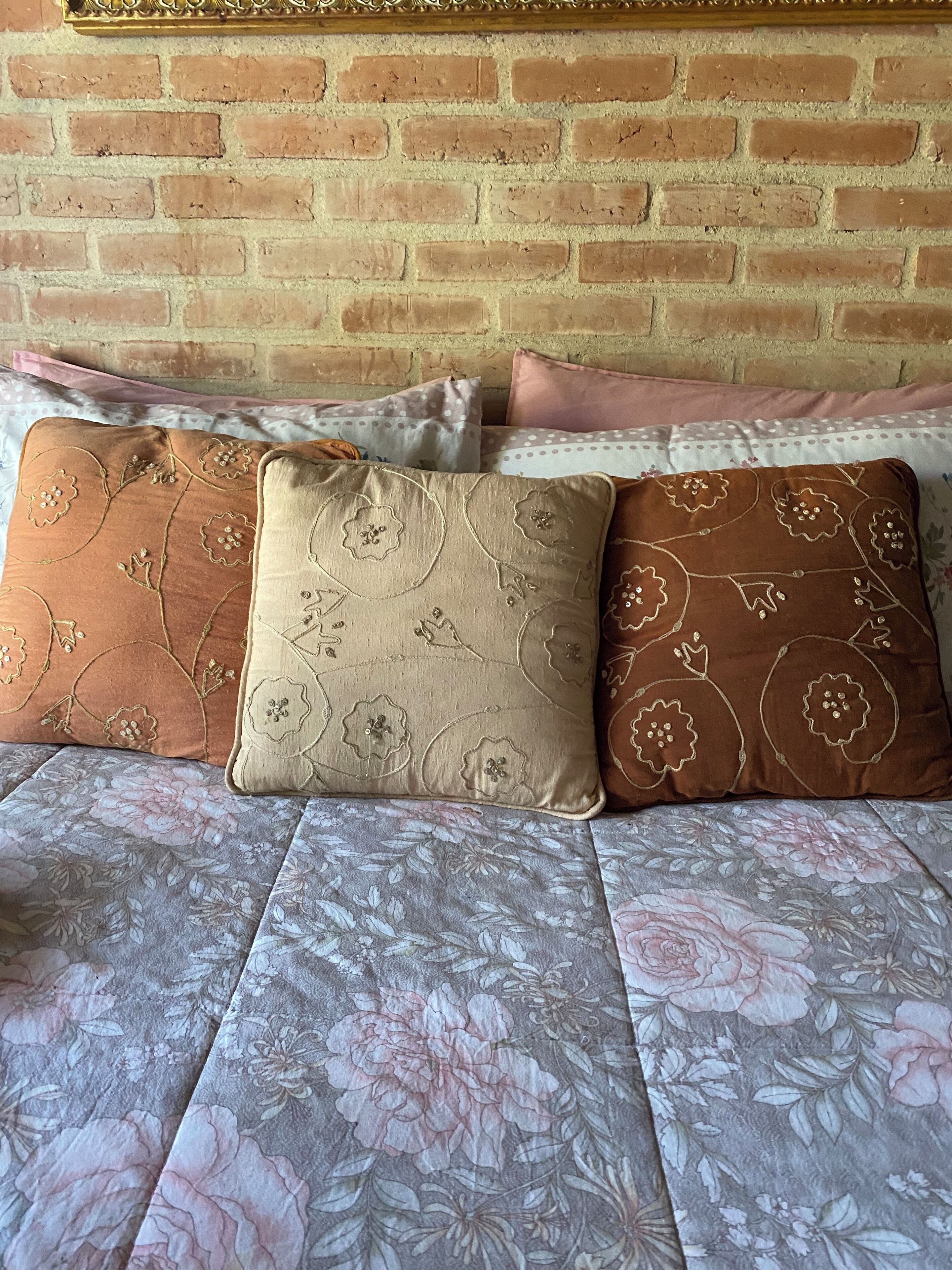 Una cama con ropa de cama de estampado floral y tres almohadones decorativos con diseños florales.