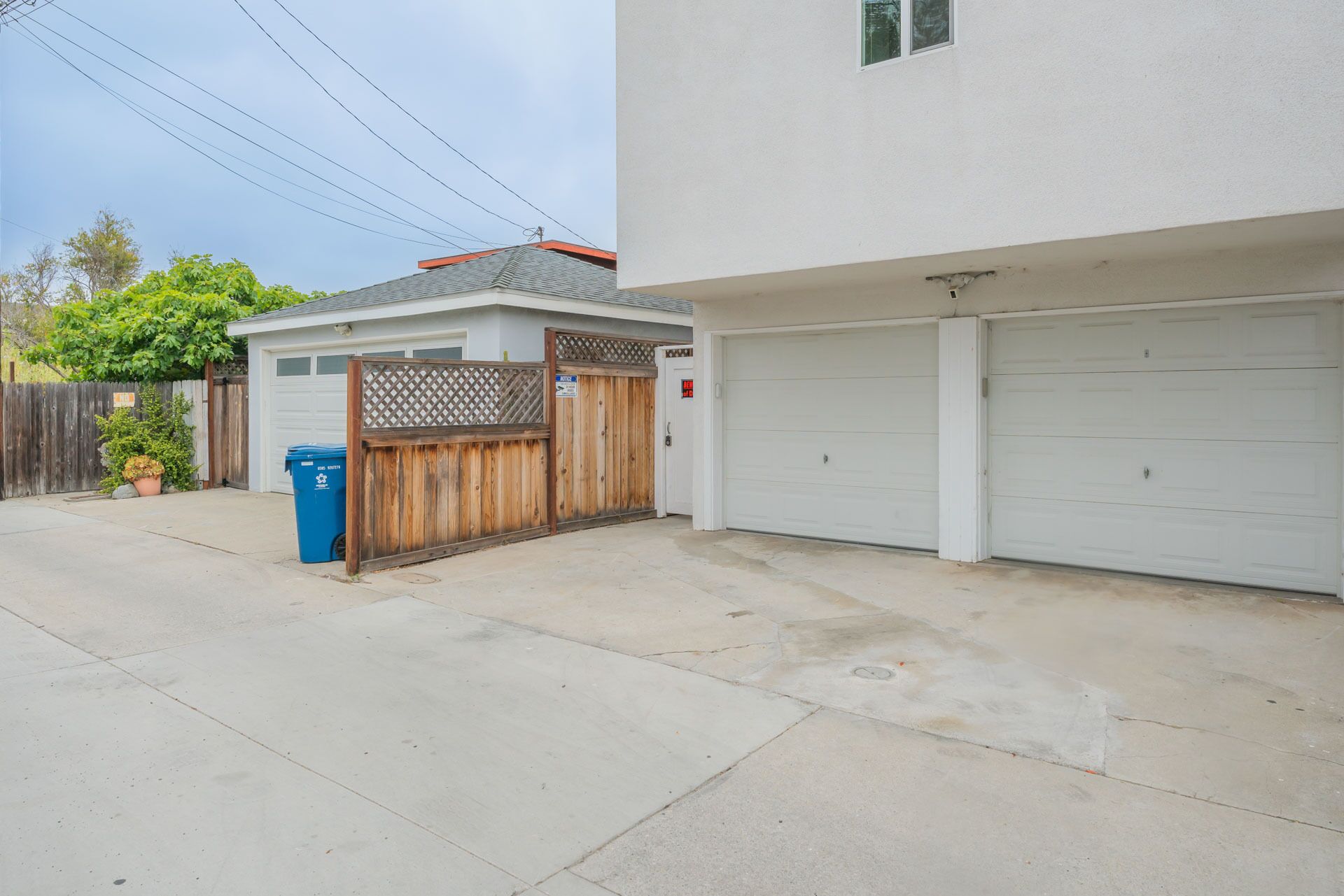 Un garage residenziale con due porte garage bianche, una recinzione in legno e un piccolo deposito con tetto spiovente.