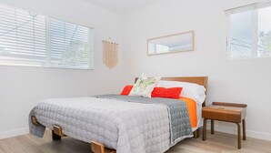 A bedroom with a bed, wooden nightstands, a wall-mounted tapestry, and a framed picture.