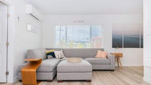 A modern living room with a grey sectional sofa, a wooden side table, and a view of the outdoors through large windows.