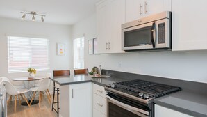A modern kitchen with white cabinets, a built-in microwave, a gas stove, and a dining area with a table and chairs.