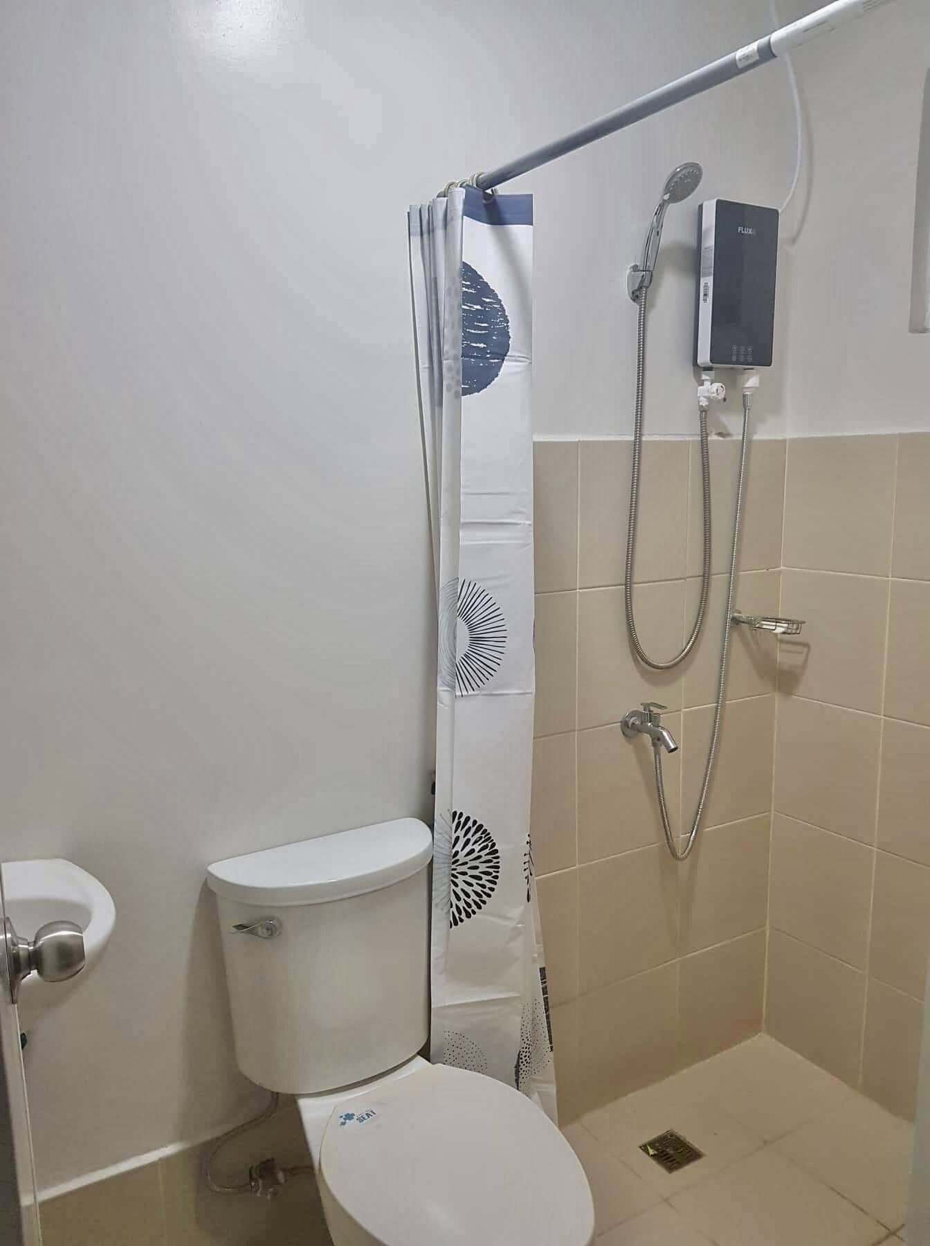 A bathroom with a toilet, a shower with a handheld showerhead, and a wall-mounted control panel.
