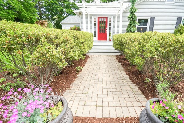 A pathway leading to a house with a red door, surrounded by well-maintained hedges and flowering plants.