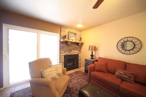 A living room with a fireplace, a sofa, a chair, and a large window.