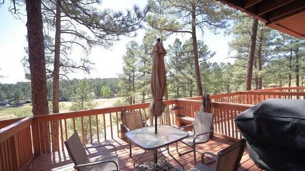 Une terrasse en bois, aménagée avec du mobilier d’extérieur, notamment des chaises et une table, et offrant une vue sur une zone boisée.