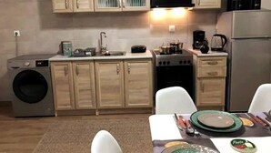 A compact kitchen with wooden cabinets, a washing machine, a stove, and a refrigerator. - 1 Bed - Sleeps 2 - Balcony - Sea View - Parking (Kalymnos)