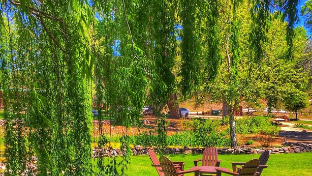 A patio area with Adirondack chairs and a table, surrounded by a stone border and lush greenery. - Views, views, views! Spacious home with Red Rock & Sunset Views. Near the river! (Clarkdale)