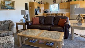 A living room with a brown leather sofa, patterned armchairs, a glass-top coffee table, and a kitchen in the background. - Views, views, views! Spacious home with Red Rock & Sunset Views. Near the river! (Clarkdale)