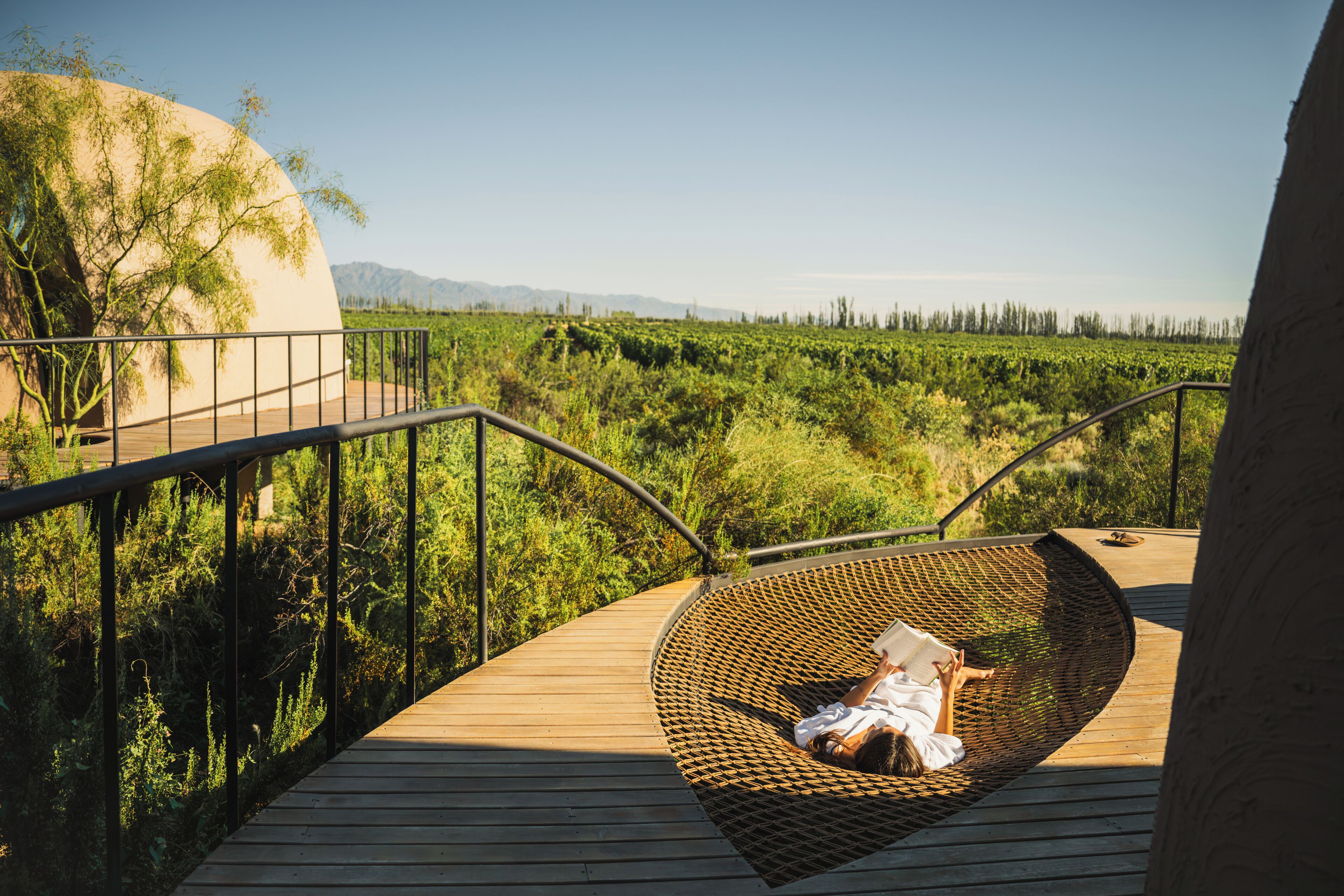 A wooden deck with a woven chair and a person reading a book.