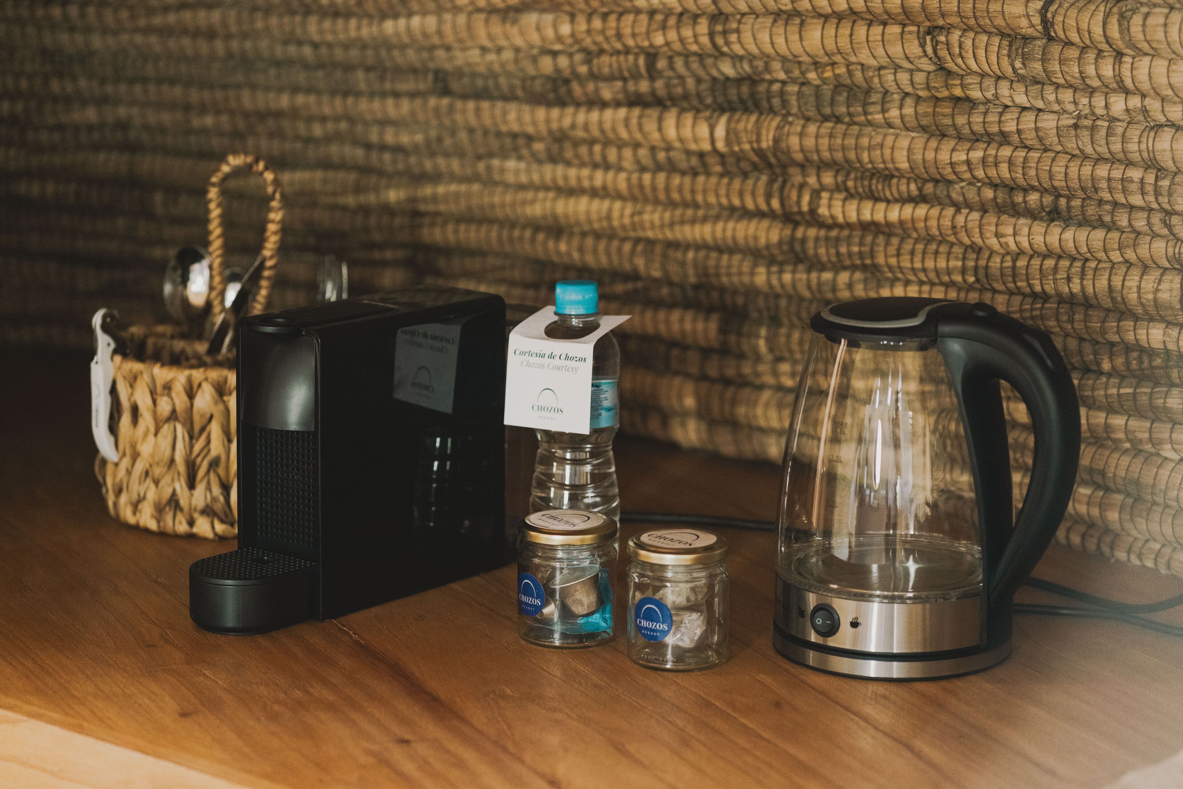 Una cafetera, dos frascos de vidrio, una botella de agua y un hervidor sobre una superficie de madera.