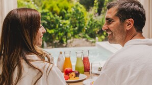 A couple seated at a table with a view of a garden and a building in the background. - Chozos Resort (Ugarteche)