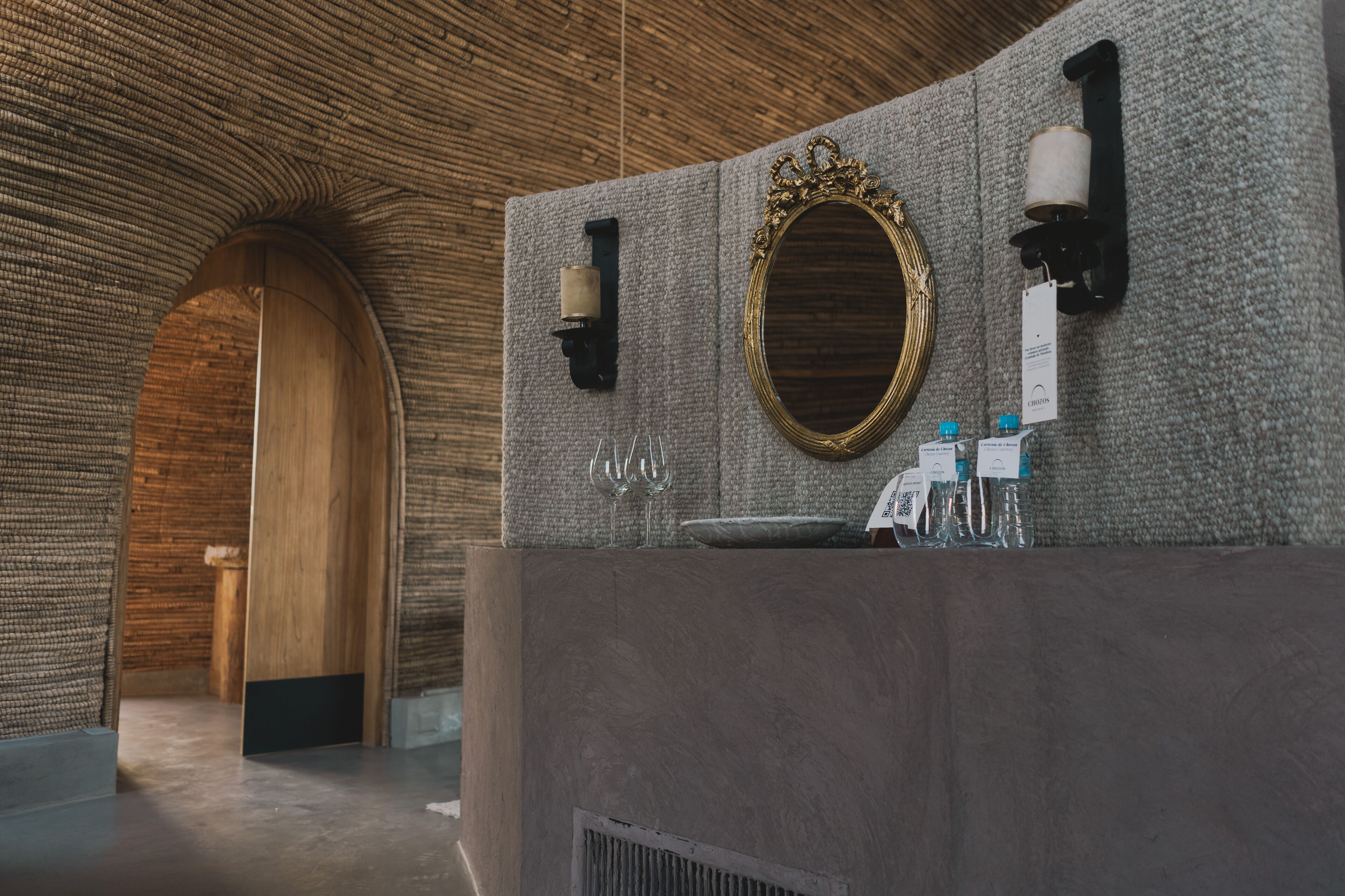 A modern bathroom with a stone wall, a wooden door, a mirror, and a sink with toiletries.