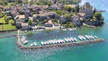 Une vue aérienne d’une ville côtière, avec ses bâtiments historiques, un port de plaisance rempli de bateaux et une vue dégagée sur la mer.