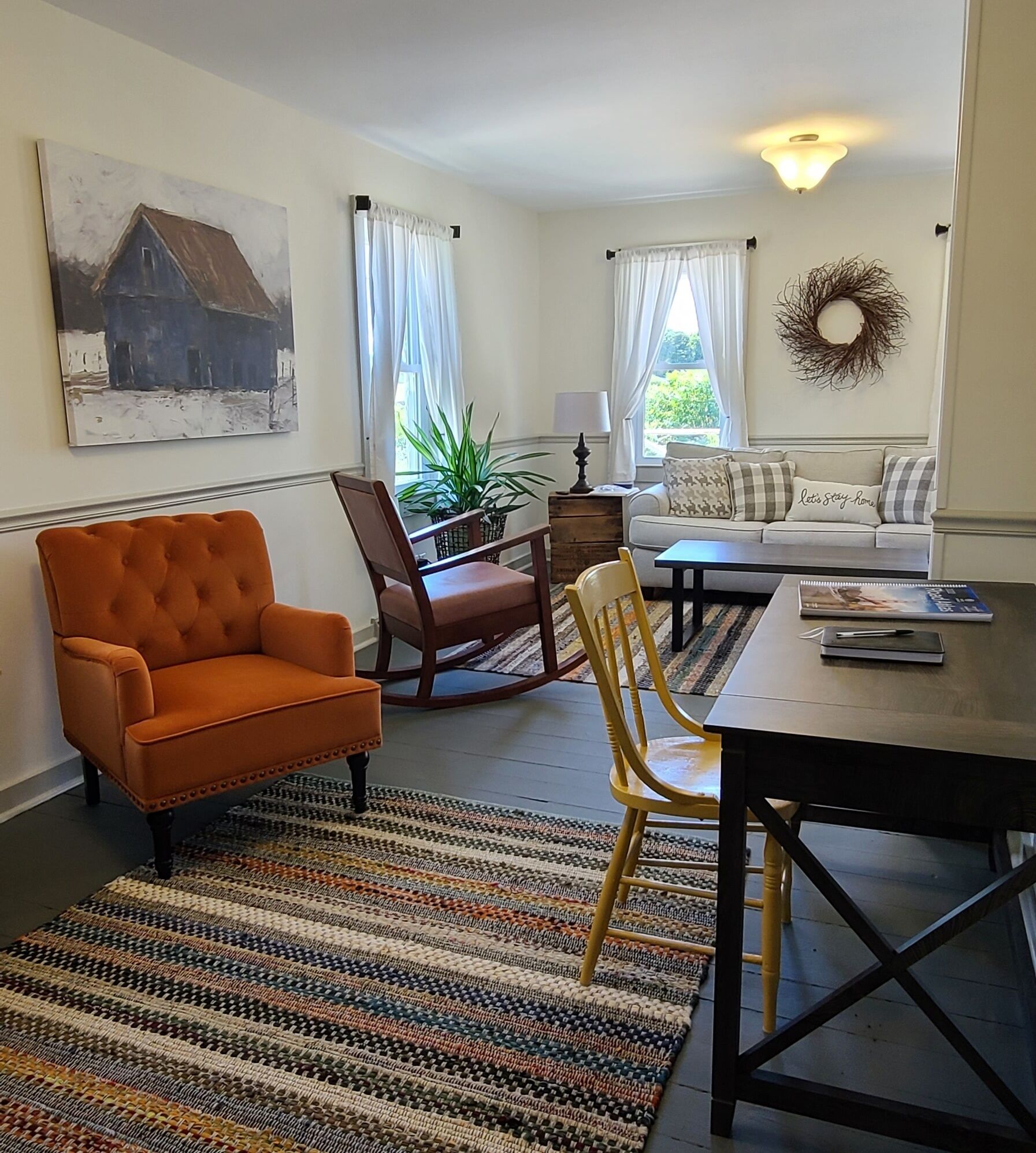 Ein Wohnzimmer mit einer Couch, einem Esstisch, einem Schaukelstuhl und einem farbenfrohen Teppich.