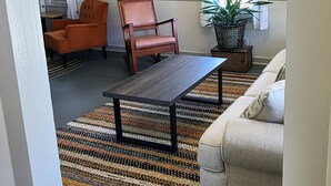 A living room with a sofa, a coffee table, an orange chair, a potted plant, and a painting on the wall.
