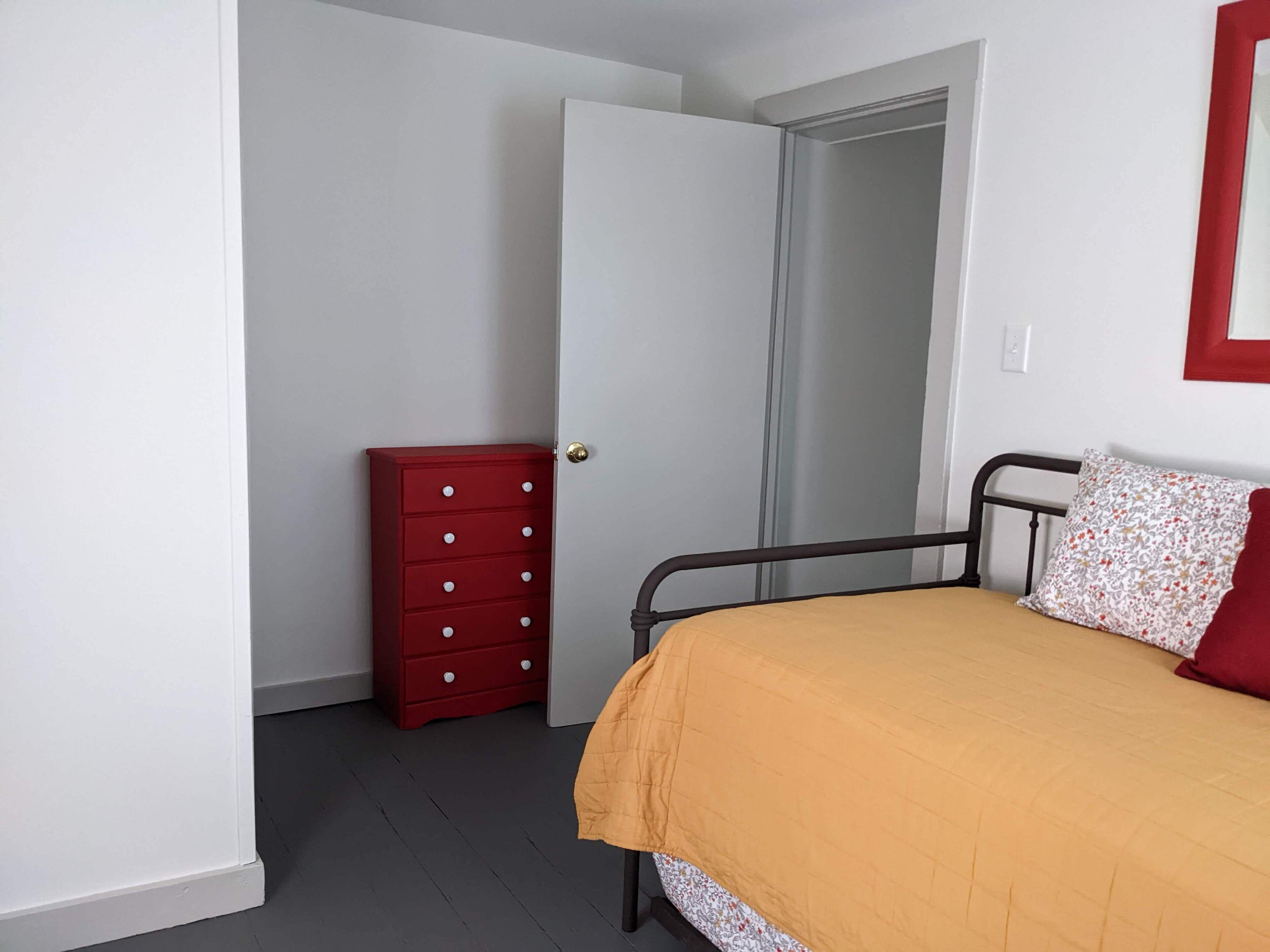 Een slaapkamer met een bed, een rode kapstok en een deur naar een inloopkast.