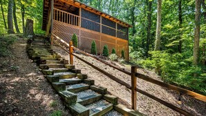 A wooden staircase leading to a cabin with a lattice facade, surrounded by dense forest. - Romantic-Hot Tub-Dog Friendly-Private-Convenient (Pigeon Forge)