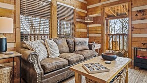A cozy log cabin interior with a leather sofa, a wooden table, and large windows with blinds. - Romantic-Hot Tub-Dog Friendly-Private-Convenient (Pigeon Forge)