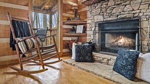 A cozy cabin interior with a stone fireplace, wooden walls, and a rocking chair. - Romantic-Hot Tub-Dog Friendly-Private-Convenient (Pigeon Forge)