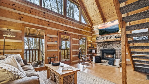 A log cabin interior with a fireplace, wooden furniture, and a stone fireplace surround. - Romantic-Hot Tub-Dog Friendly-Private-Convenient (Pigeon Forge)