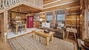 A rustic cabin interior with a wooden dining area, a sofa, and a staircase leading to an upper level. - Romantic-Hot Tub-Dog Friendly-Private-Convenient (Pigeon Forge)