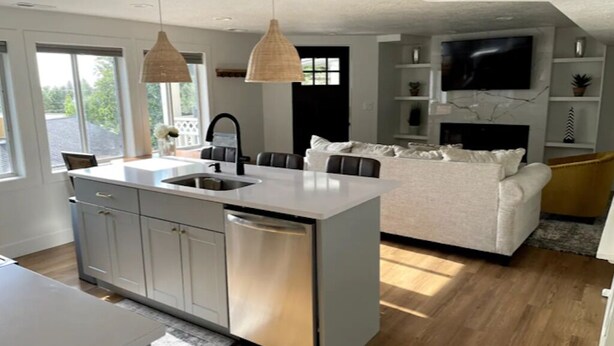 A modern kitchen with a central island, built-in cabinets, and a dishwasher. There is a dining area with a table and chairs, and a living space with a sofa and a TV. - Lovely 1-Bdrm Apt w/ Hot Tub - 5 mins from Canyons (Cottonwood Heights)