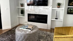 A living room with a flat-screen TV mounted on a white wall, a fireplace below, and a yellow armchair. - Lovely 1-Bdrm Apt w/ Hot Tub - 5 mins from Canyons (Cottonwood Heights)