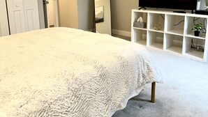 A bedroom with a large bed, a ceiling fan, a TV, a mirror, and a white shelving unit. - Romantic Two Bedroom Condo (Crofton)