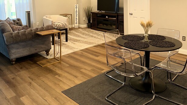 A modern living room with a sofa, a coffee table, a TV, and a dining area with chairs and a table. - Romantic Two Bedroom Condo (Crofton)