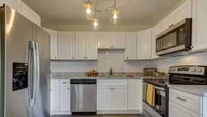 A modern kitchen with white cabinets, stainless steel appliances, and a granite countertop. - Romantic Two Bedroom Condo (Crofton)
