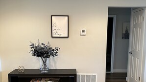 A hallway with a black console table, a framed motivational quote, a thermostat, and a door labeled "home". - Romantic Two Bedroom Condo (Crofton)